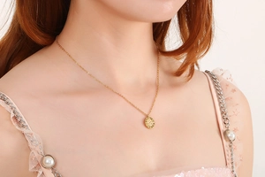 Close-up of a gold circular textured pendant necklace worn by a model in pink sequins