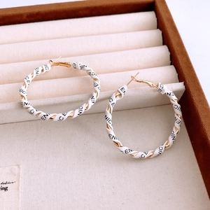 Close-up of gold metal and white leather braided hoop earrings with letter print