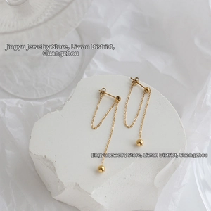 Close-up of gold chain tassel earrings with gold beads on a white minimalist background