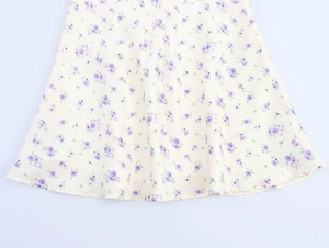 Détail d'une robe en satin jaune clair avec imprimé floral violet et ourlet fluide
