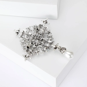 Elegant silver baroque cross brooch with a hanging white pearl on a clean white background