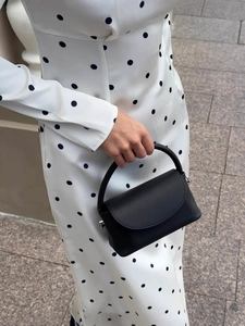 Elegant black matte leather mini handbag with top handle and polka dot dress contrast