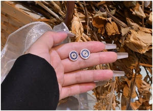 Detailed macro shot of blue and white evil eye stud earrings held in hand