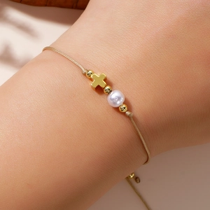 Detail shot of golden braided rope bracelet with metallic cross and white pearl on wrist