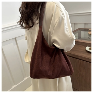 Side view of a vintage brown matte suede shoulder bag worn by a model in a minimal room