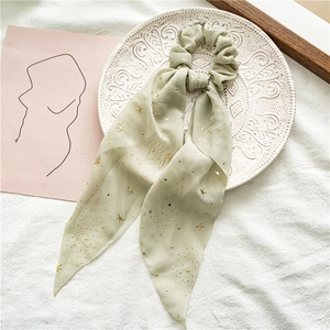 Close-up of light green star-sequined chiffon scrunchie with long ribbon on white fabric