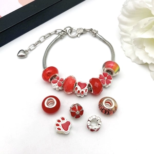 Silver snake chain bracelet with red themed beads and charms on elegant white background