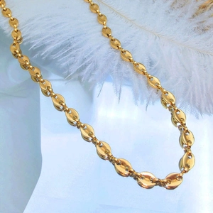 Elegant gold coffee bean link necklace displayed on white feathers and mirrors