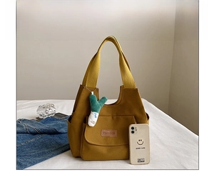 Detail view of yellow canvas tote bag with front pocket, fashion label and plush charm