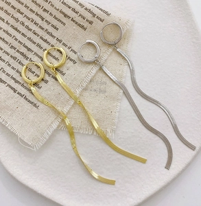 Detailed view of long gold and silver snake chain tassel earrings on elegant fabric