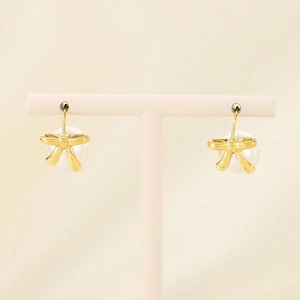 Detail of golden bow earrings with white pearls hanging on a white jewelry stand
