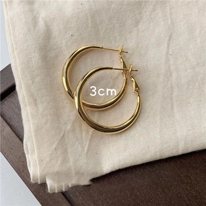 Macro shot of 3cm polished gold hoop earrings resting on a textured linen fabric