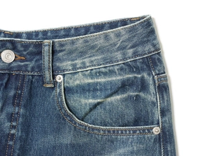 Detail of high-density metal button and reinforced stitching on dark blue denim jeans