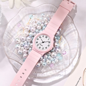 Close-up of pink quartz watch with silicone strap on a shell tray filled with pearls