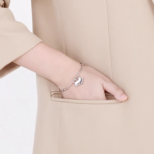 Détail d'un bracelet en argent avec pendentif chat porté sur une poche de costume kaki