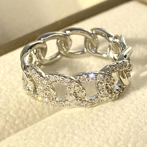 Macro shot of silver curb chain ring with pave-set zircons on a beige velvet jewelry box