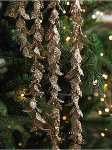 Close-up of champagne gold glittery leaf pick hanging on a sparkling Christmas tree