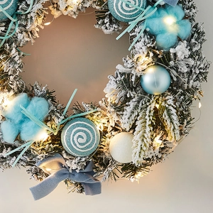 Blue and white Christmas wreath with cotton, velvet bow and warm LED lights on pine needles