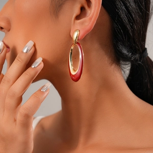 Close-up of gold and red oval enamel earrings worn by a model for a chic style