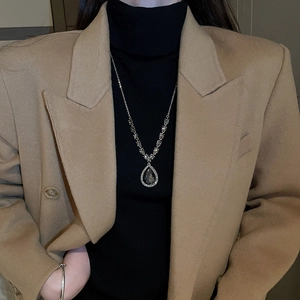 Détail d'un collier en V avec pendentif goutte et diamants sur un pull à col roulé