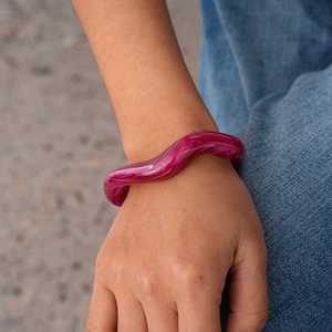 Detail view of wavy acrylic bangle with berry red and white marble texture on wrist