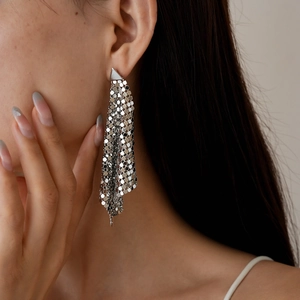 Close-up of silver geometric metal mesh fringe earrings worn by a model