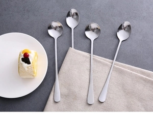Quattro cucchiai in acciaio inox con manico lungo su tovagliolo con dessert