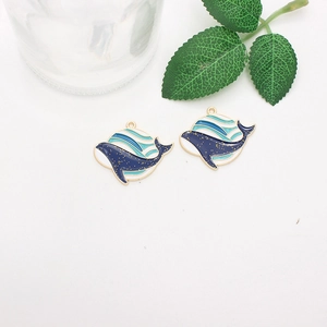 Detail of whale-shaped enamel charms with blue ocean scenes and golden glitter edges