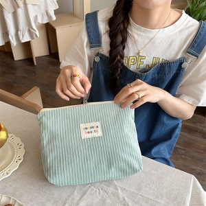 Light green corduroy makeup bag with embroidery label held by a model in a cozy setting