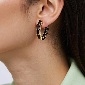 Close-up of a model wearing a gold hoop earring with an inlaid black zircon gemstone