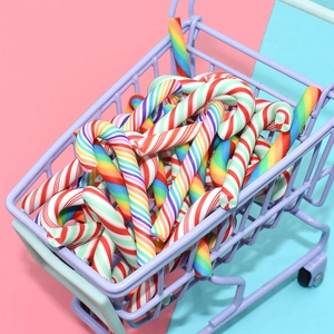 Rainbow candy canes in a mini purple shopping cart on a pastel pink and blue background