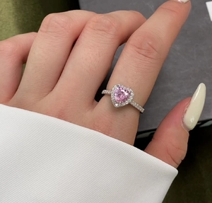Macro view of pink heart-cut gemstone ring with micropavé zircon setting on female finger