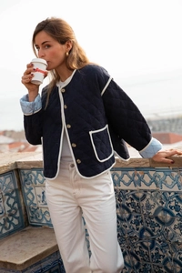 Detail of navy quilted jacket with white contrast trim and front pockets on model