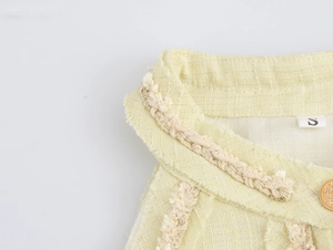 Détail du tissu en tweed avec bordure dorée et franges sur la robe jaune chic