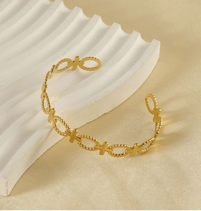 Detailed shot of a gold open cuff bracelet with hollow cross patterns on white stone