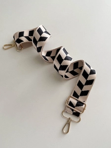 Detail of black and white geometric fabric bag strap with golden metal clasps