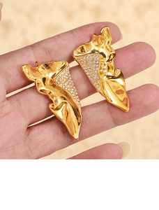 Macro detail of gold-finish wing earrings with pleated texture and sparkling rhinestones