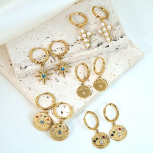 Detail view of gold hoop earrings with pearl cross, star, and evil eye charms