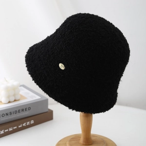 Detail of soft black lamb wool bucket hat with elegant gold metal logo plate on wood stand