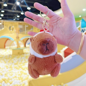 Detailed close-up of brown plush capybara keychain with white scarf and gold metal clasp
