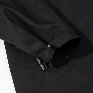 Detail of black trench coat cuff with metal snap button and leather trim accents