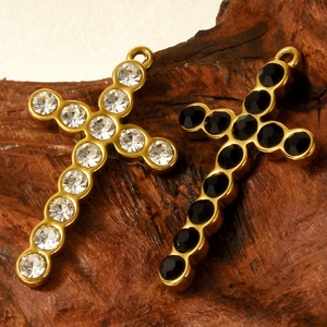 304 stainless steel cross pendants with inlaid clear and black gems on wood surface