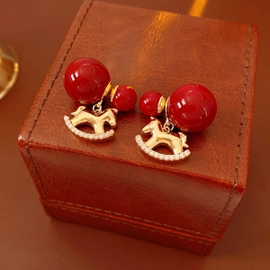 Detail of gold plated rocking horse earrings with red beads and zircon on leather box