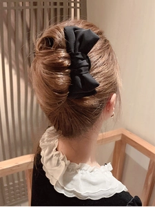 Close-up of a large black fabric bow hair clip styled on a refined bun hairstyle