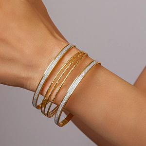 Detail of layered gold and sequin finish bangles worn as a 5-piece minimalist set