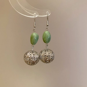 Détail de boucles d'oreilles boules argentées ajourées avec perles ovales en résine verte