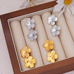 Five-petal flower stud earrings in gold and silver finish displayed on wooden jewelry box