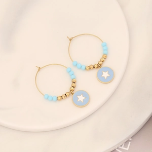 Golden earrings with blue star charms and beads on a ceramic plate, minimalist style