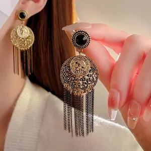 Vintage gold tassel earrings with black gemstone and engraved coin detail on model