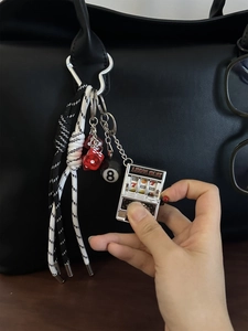 Detail von Lucky Slot und 8-Ball Schlüsselanhänger an einer schwarzen Modetasche